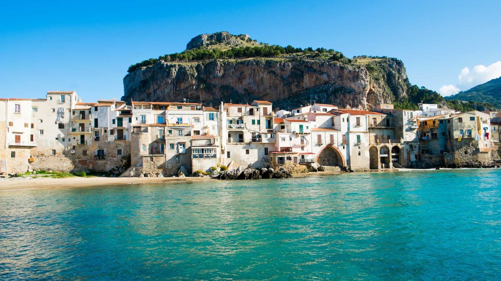 Vista panoramica di un borgo italiano su un'isola, con case colorate e mare cristallino.